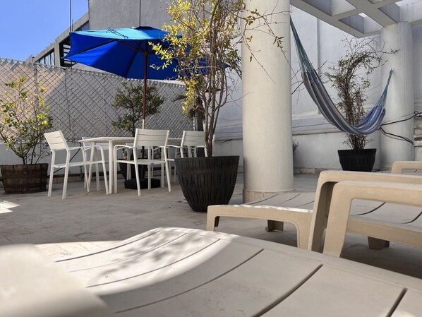 An outdoor seating area with white chairs and tables, a blue umbrella, and a hammock.