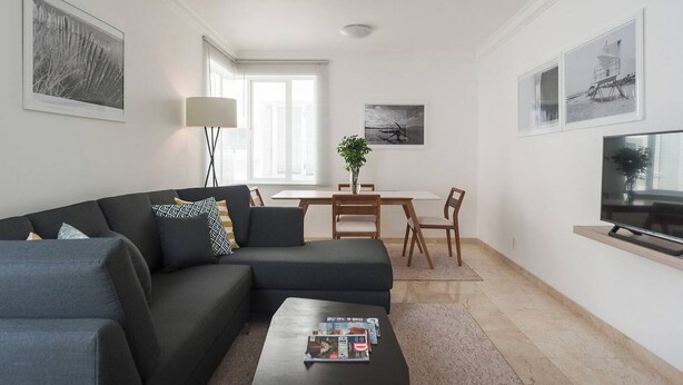 A modern living room with a sectional sofa, a coffee table with magazines, a TV on a stand, and a dining area with a table and chairs. - Condesa Residence Campeche 8 (Ciudad de México)