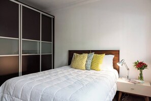 A hotel room with a bed, a nightstand, a lamp, and a vase with flowers.