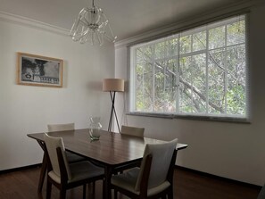 Un coin repas avec une table et des chaises en bois, un lampadaire et une grande fenêtre équipée de stores.
