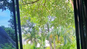 A bed with a view of a lush garden through a window. - Cashewnut Tree Resort (Ko Lanta)