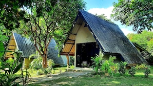 A traditional thatched-roof hut with a concrete foundation, surrounded by lush greenery and trees. - Cashewnut Tree Resort (Ko Lanta)