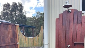 A wooden gate with a metal handle, a white pipe, and a small white platform leading to a door.