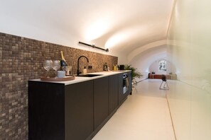 A modern kitchen with a brick backsplash, a long counter, and a view of the adjacent living area.
