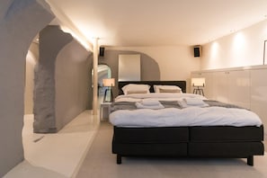 A modern bedroom with a dark-colored bed, a nightstand, a lamp, and a wardrobe.