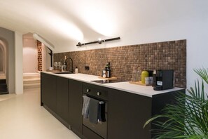 A modern kitchen with a large island, dark cabinetry, and a brick backsplash.