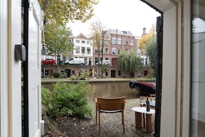 A view from a room with a window overlooking a canal, featuring a wooden chair and table, and buildings in the background. - Canallofts - The Wharf Wellness (Utrecht)
