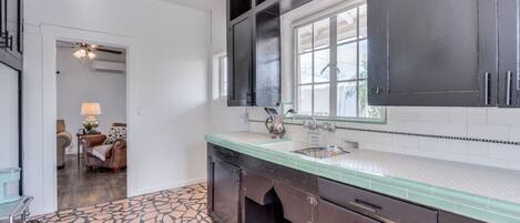 Cocina moderna con armarios oscuros, encimera verde y un ventanal amplio.