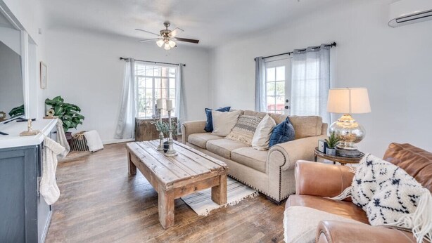 A spacious living room with a wooden coffee table, beige sofa, and a leather armchair. There are ceiling fans, a lamp, and a window with curtains. - 1926 Original Firehouse / Close to U of A / Loft (Tucson)