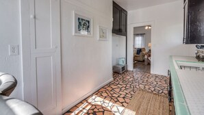 A hallway with white walls, a tiled floor, and a kitchen area with a stove and cabinets. - 1926 Original Firehouse / Close to U of A / Loft (Tucson)