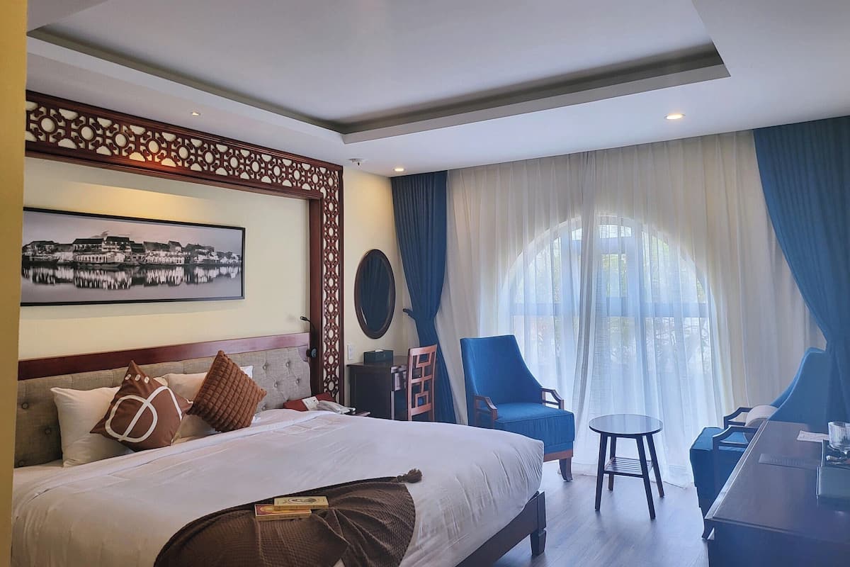 Ein Hotelzimmer mit Bett, Schreibtisch, Stuhl, großem Fenster mit Vorhängen, Wand-Fernseher und dekorativem Wandpaneel.