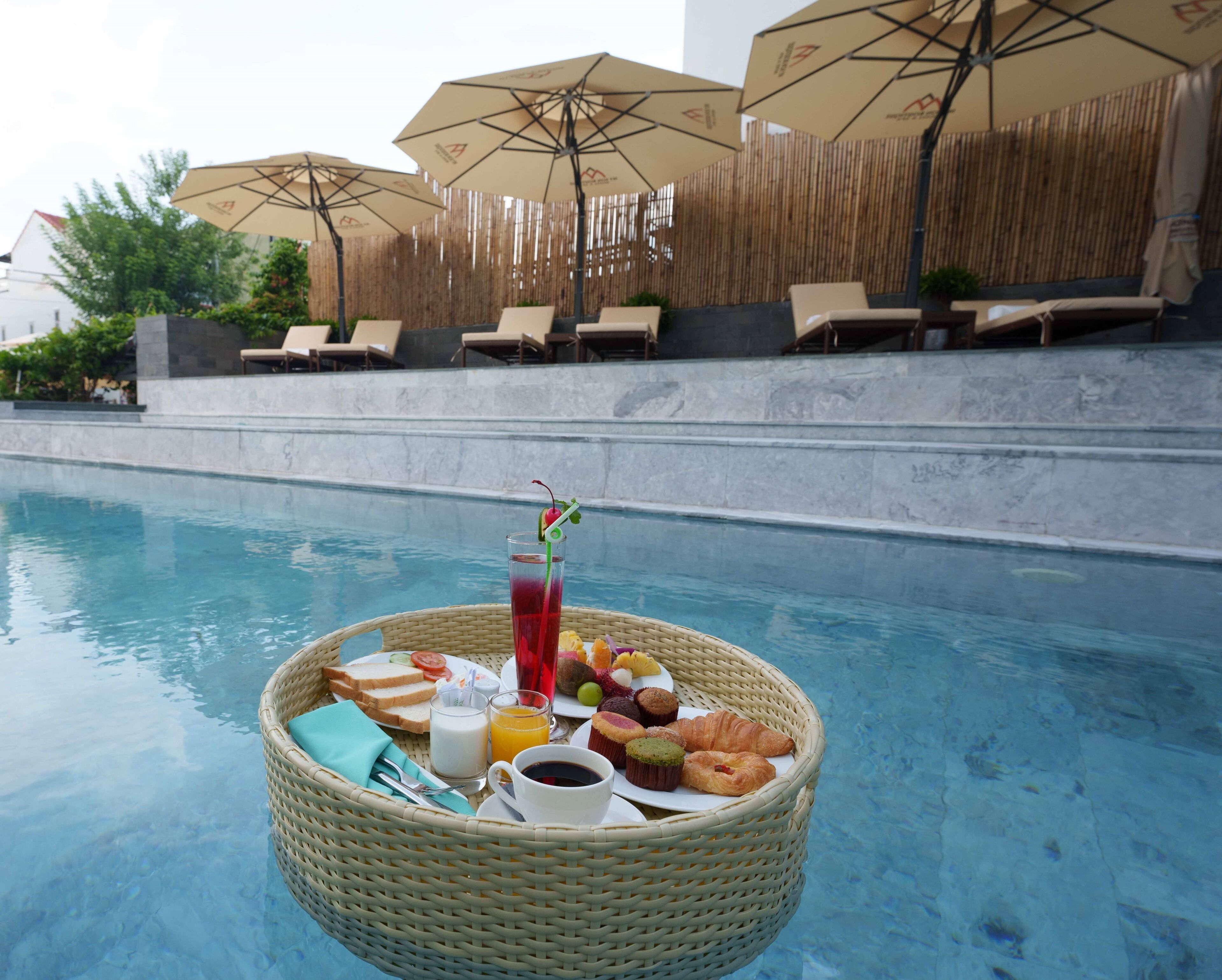 Ein Frühstück am Pool mit einem Korbkorb, der Speisen und Getränke enthält, umgeben von Liegestühlen und Sonnenschirmen.
