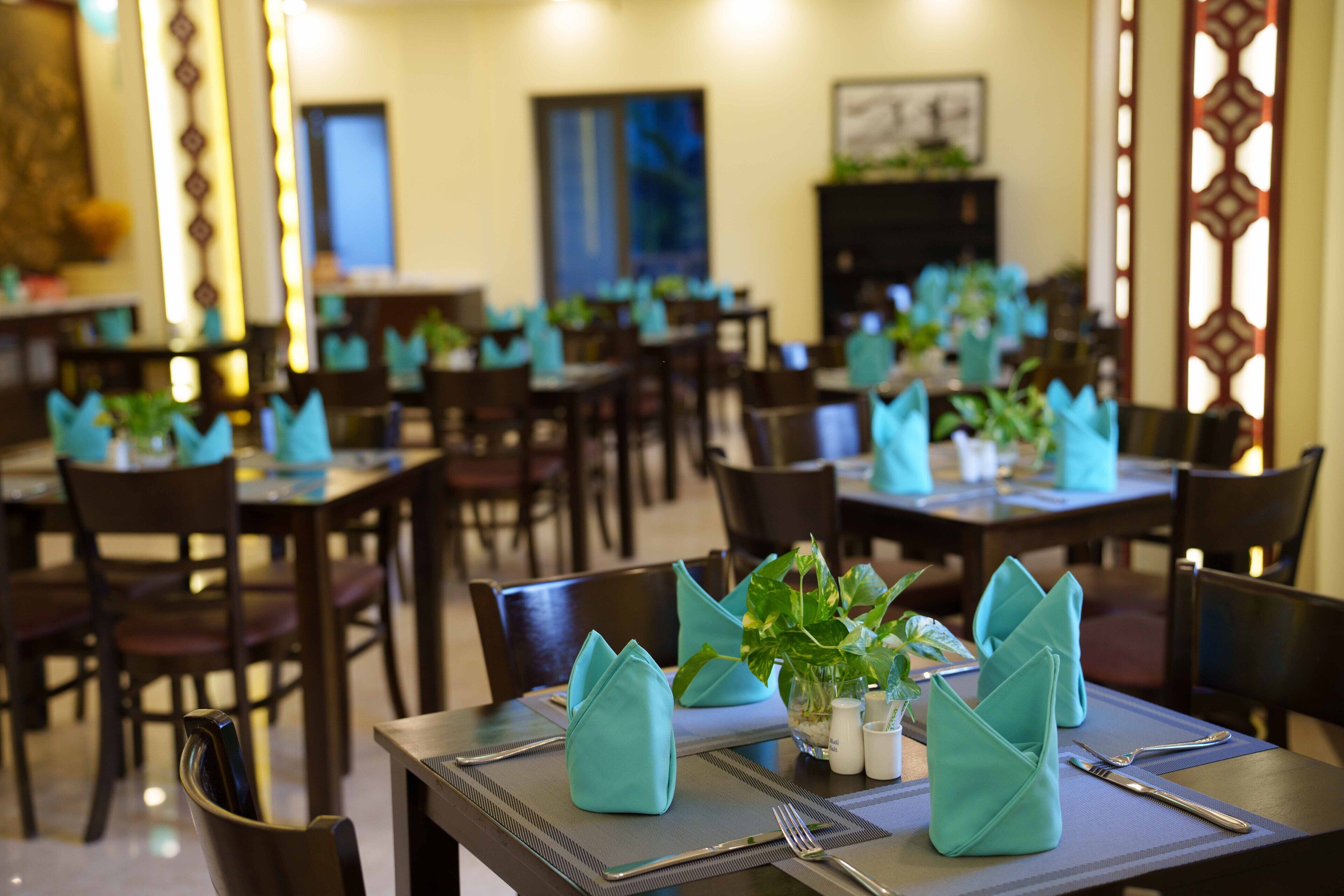 Een restaurant met tafels gedekt met blauwe servetten, bestek en kleine potplanten.