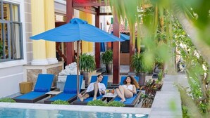 Een zwembadgedeelte met ligstoelen en parasols, omgeven door groen en architectonische zuilen.