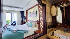 Hotelkamer met een groot bed, een zithoek met een stoel en een tafel, een badkamer met een wastafel en spiegel, en uitzicht op het omliggende landschap.