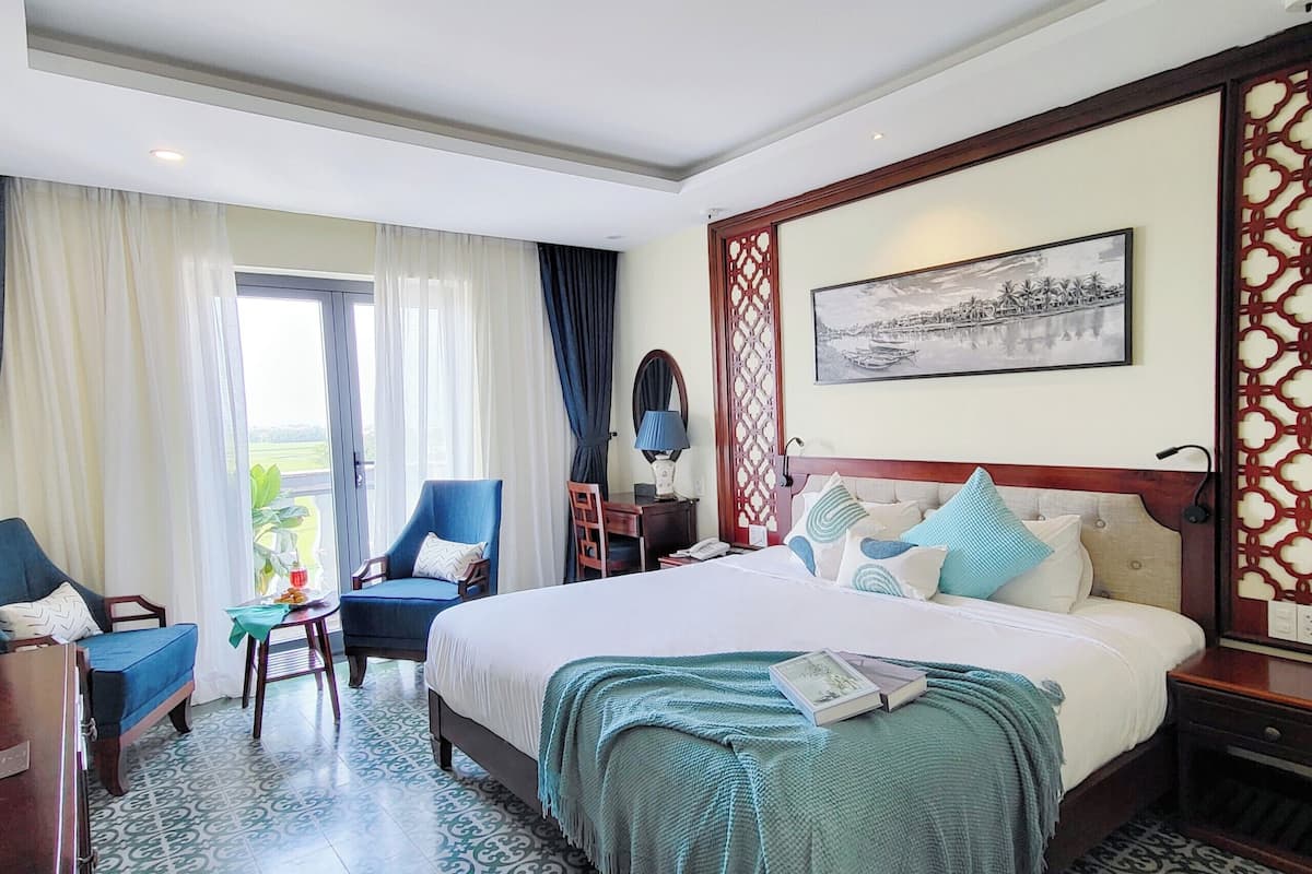 Ein Hotelzimmer mit einem großen Bett, einem Schreibtisch, einem Stuhl und einem Fenster mit Vorhängen.