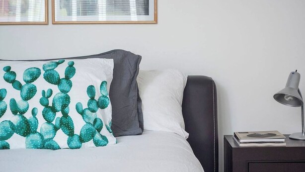 A neatly made bed with a cactus-themed pillow, a bedside lamp, and a framed picture on the wall. - Condesa Residence Campeche 11 (Ciudad de México)