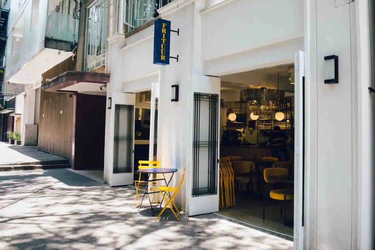 Une vue de rue d’un immeuble dont on aperçoit l’entrée et au-dessus de laquelle est affiché un panneau.