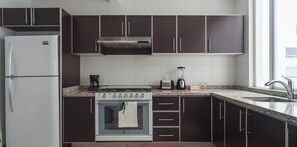 Une cuisine moderne avec des meubles de couleur sombre, un réfrigérateur blanc, une cuisinière et un évier.