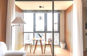 A modern room with a dining table and chairs, a lamp, and a view of the city through large windows. - Bona Travel Haeundae (Busan)