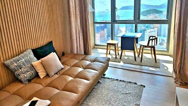 Un salon moderne avec un canapé en cuir, une petite table et une vue sur le paysage urbain à travers de grandes fenêtres.