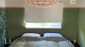 A bed with a grey bedspread, a wooden hanging light fixture, and a window with a white blind.
