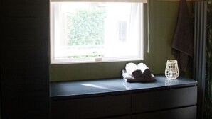 A bathroom with a window, a towel rack, and a small table with a towel and a decorative item.