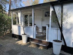 A covered porch with a bench, a small table, and a potted tree. - Stacaravan Chalet te Huur Hoenderloo Park Veluwshof (Hoenderloo)