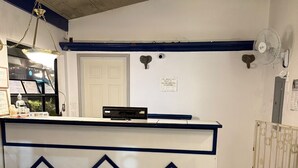 Un área de recepción con mostrador, puerta, ventilador de pared y suelo de baldosas.