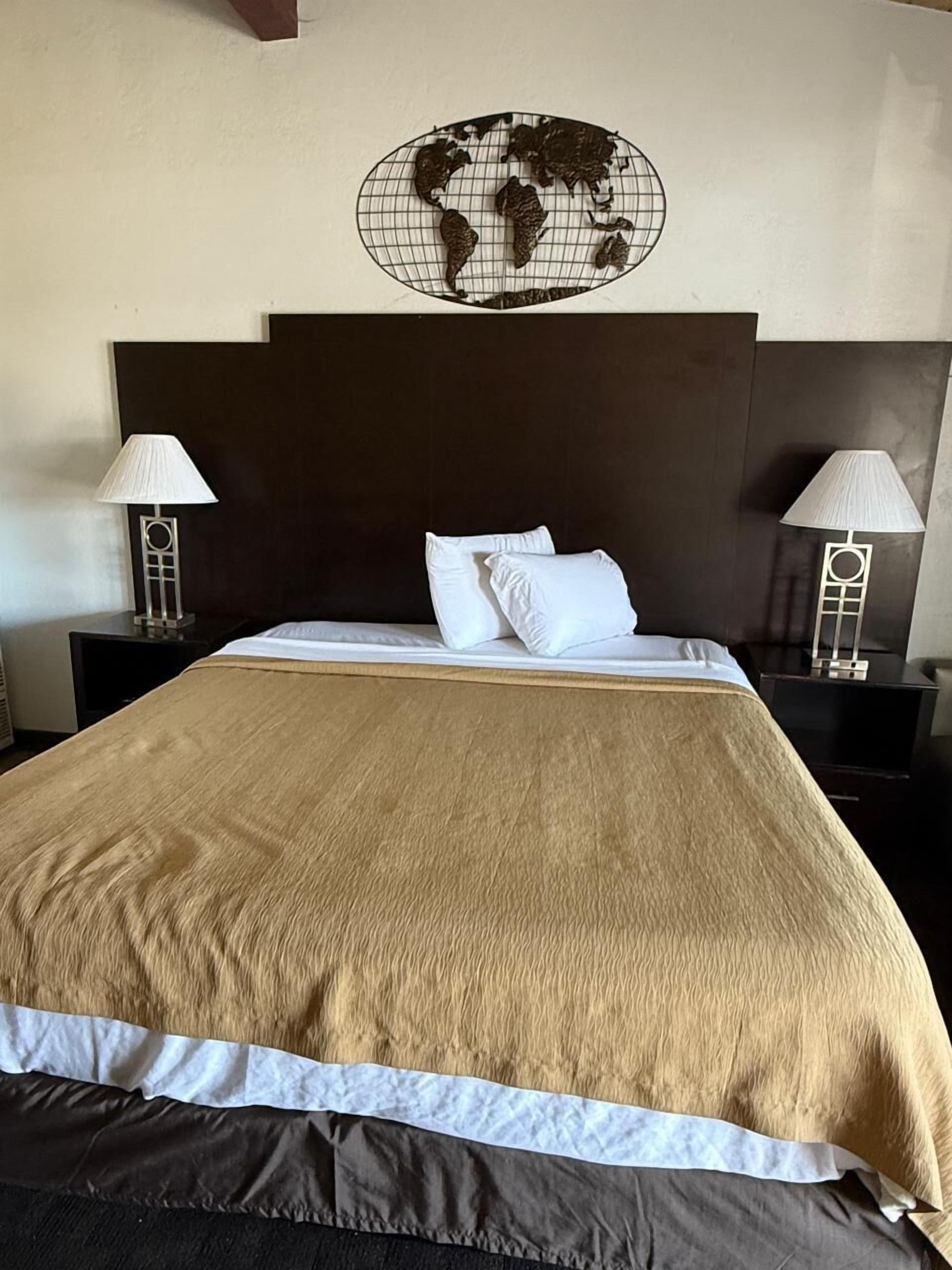 A hotel room with a large bed, two bedside tables with lamps, a world map on the wall, and a dark headboard.