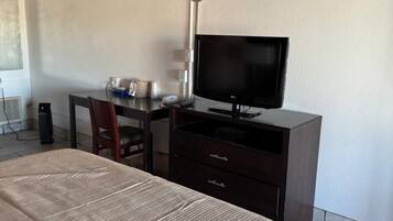 Quarto de hotel com uma cama, uma mesa de trabalho com televisão, uma cadeira e um abajur.