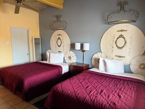 A hotel room with two beds, each with a red bedspread, a bedside table with two lamps, and decorative wall sconces. - Cinderella Motel (Hollister)