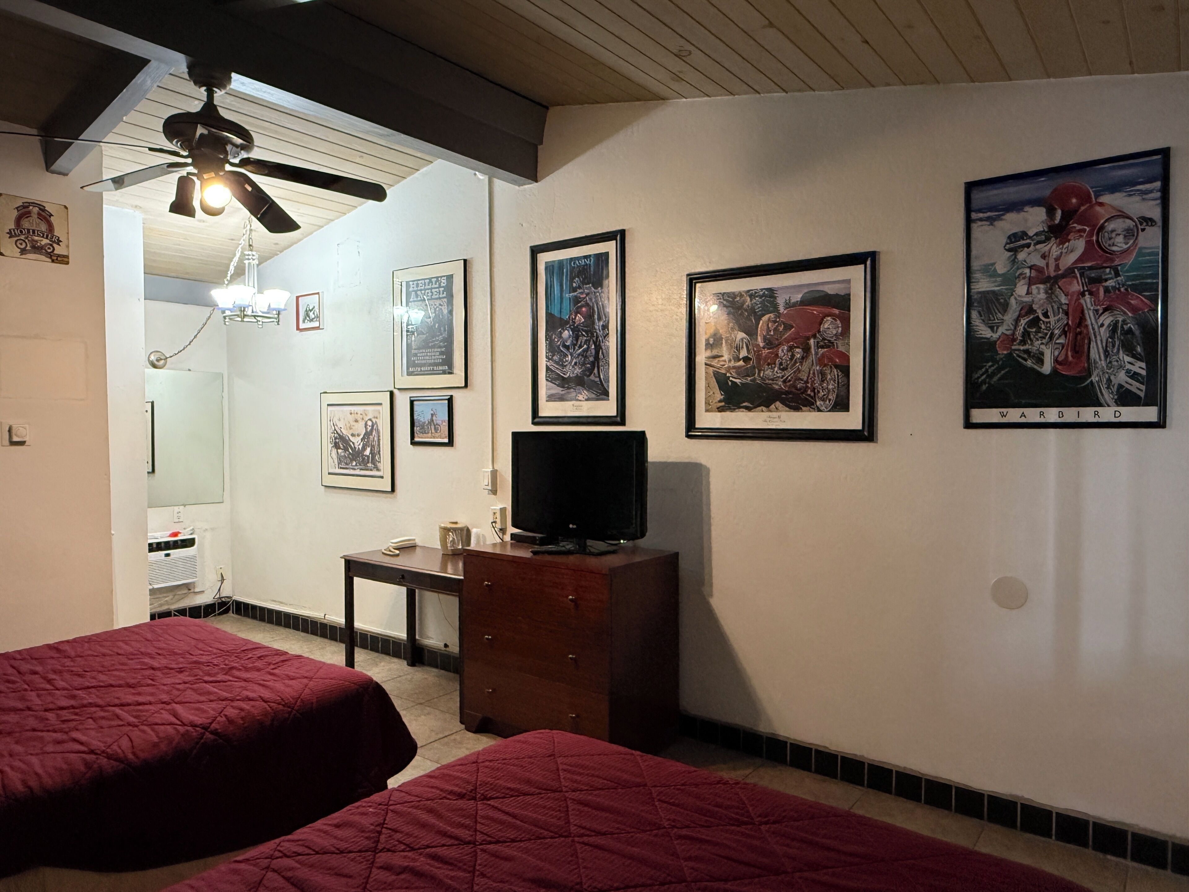 A room with two beds, a ceiling fan, a TV, and several framed pictures on the wall.