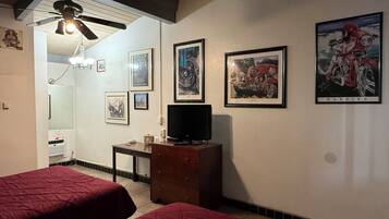 A room with two beds, a ceiling fan, a TV, and several framed pictures on the wall.