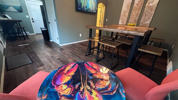 Comedor con una mesa redonda, un cuadro abstracto de colores, sillas rojas y una barra de madera.