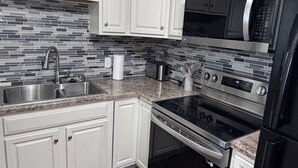 Una cocina con armarios blancos, un lavamanos de acero inoxidable, un microondas, un horno y un refrigerador negro.