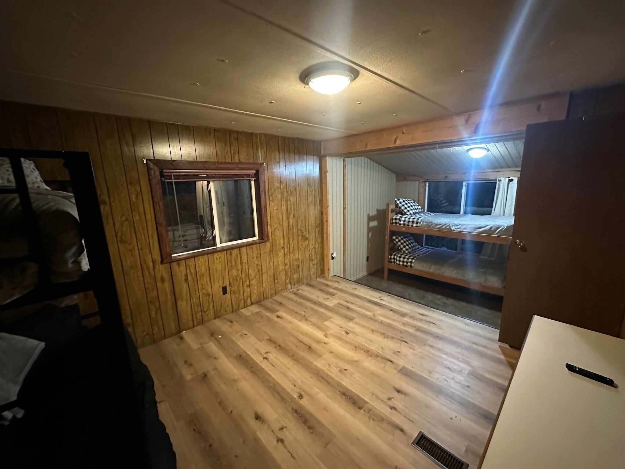 Quarto com paredes e chão de madeira, uma beliche, uma janela e uma porta.