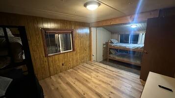 Quarto com paredes e chão de madeira, uma beliche, uma janela e uma porta.