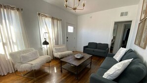 A living room with a wooden floor, a dark grey sofa, a white furry chair, a black floor lamp, and a coffee table.