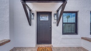 A house entrance with a dark brown door, a number '115' above it, and a window to the right.