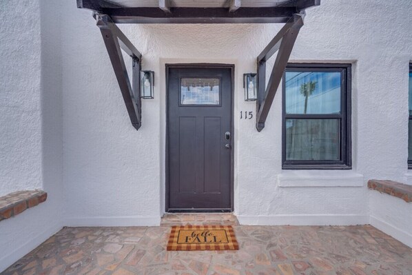 Une entrée de maison avec une porte de couleur brun foncé, le numéro « 115 » au-dessus, et une fenêtre sur la droite.