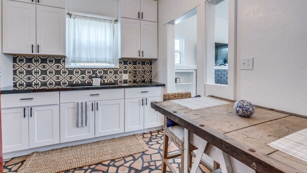 A modern kitchen with white cabinets, patterned backsplash, and a wooden table with a vase.