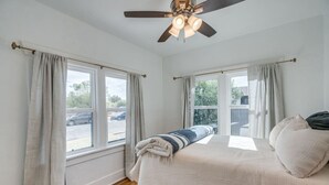 A bedroom with a bed, a ceiling fan, and three windows with curtains.