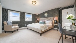 A bedroom with a large bed, two bedside tables, a chair, and a desk with a vase of flowers.