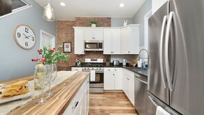 A modern kitchen with white cabinets, a stainless steel refrigerator, and a wooden countertop.
