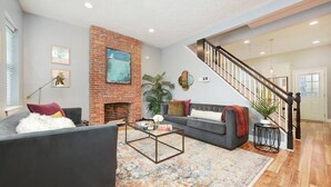 A spacious living room with a brick fireplace, a gray sofa, a coffee table, and a staircase leading to another level.