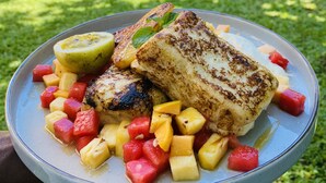 A plate of grilled fish with mango and pineapple chunks, held over a grassy area. - SURF N SPICE (Dikwella)