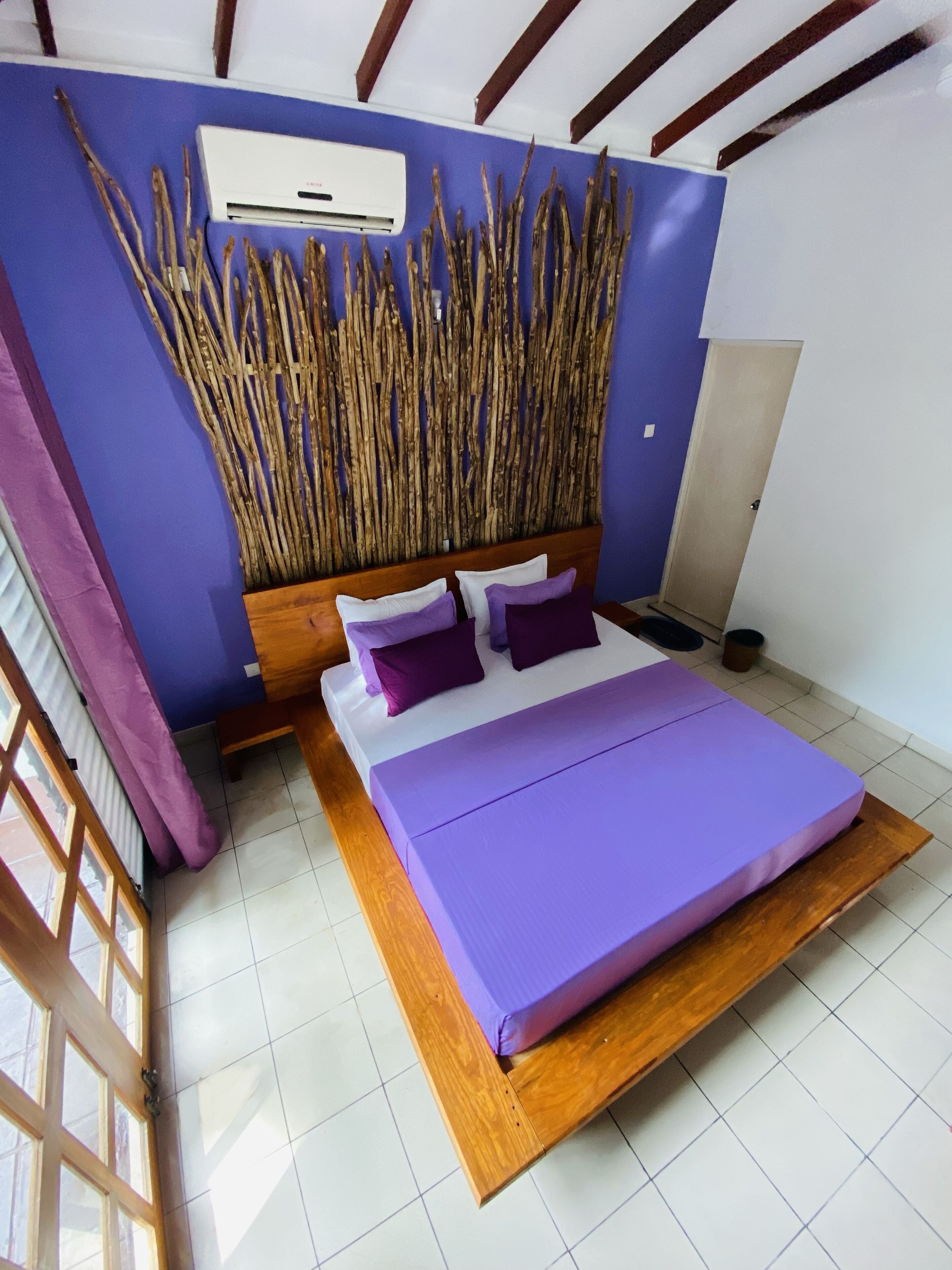 A modern bedroom with a bed, purple bedding, a wooden headboard, and a decorative wall panel.