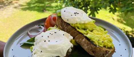 En tallerken med to åbne sandwiches, den ene med avocado og den anden med et lyst fyld, muligvis pocherede æg, på en keramikskål.