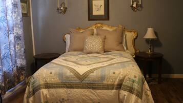 Une chambre à coucher avec un lit, une table de chevet, une lampe, un tableau encadré au mur et une fenêtre avec des rideaux.